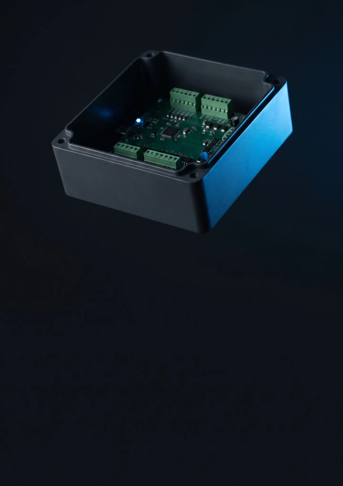 An anthracite control enclosure with its lid off, a circuit board with green terminal blocks inside, a blue light along its edge